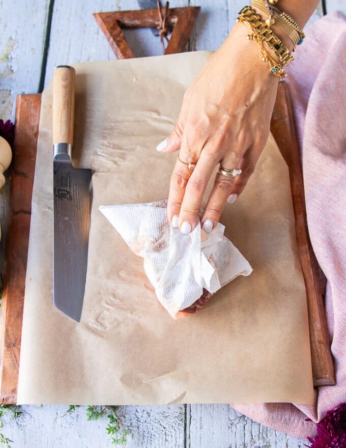 A hand pat drying the piece of beef tenderloin to make sure no moisture is on the surface