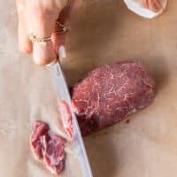 a hand holding a very sharp knife to cut thin slices of the tenderloin