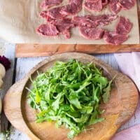 Arranging the carpaccio starts by placing the arugula in the middle of the serving middle.