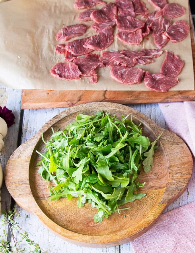 Arranging the carpaccio starts by placing the arugula in the middle of the serving middle. 