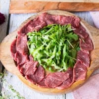 The sliced beef tenderloin arranged around the arugula slightly overlapping in the serving plate