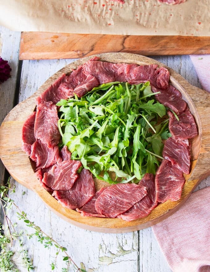 The sliced beef tenderloin arranged around the arugula slightly overlapping in the serving plate