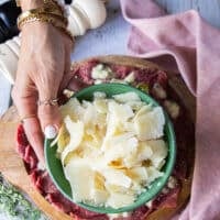 A hand holding a plate of parmesan shavings to garnish the beef carpaccio