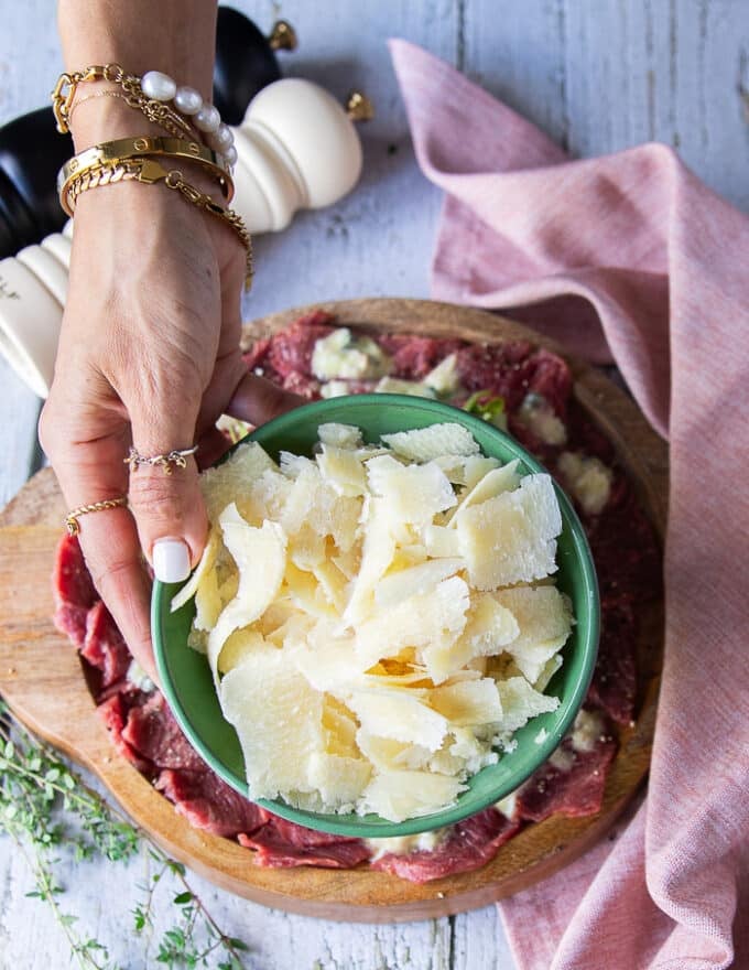 A hand holding a plate of parmesan shavings to garnish the beef carpaccio