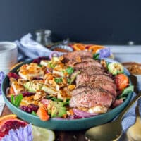 A close up plate of the sliced lamb loin and lamb sirloin over a bed of halloumi salad and citrus segments , avocados, almonds, onions and a citrus honey dressing