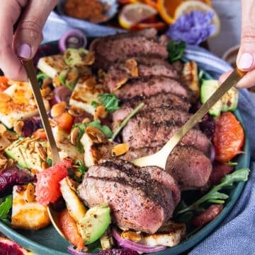 A hand serving the lamb loin recipe and salad using two spoons showing close up the salad and lamb