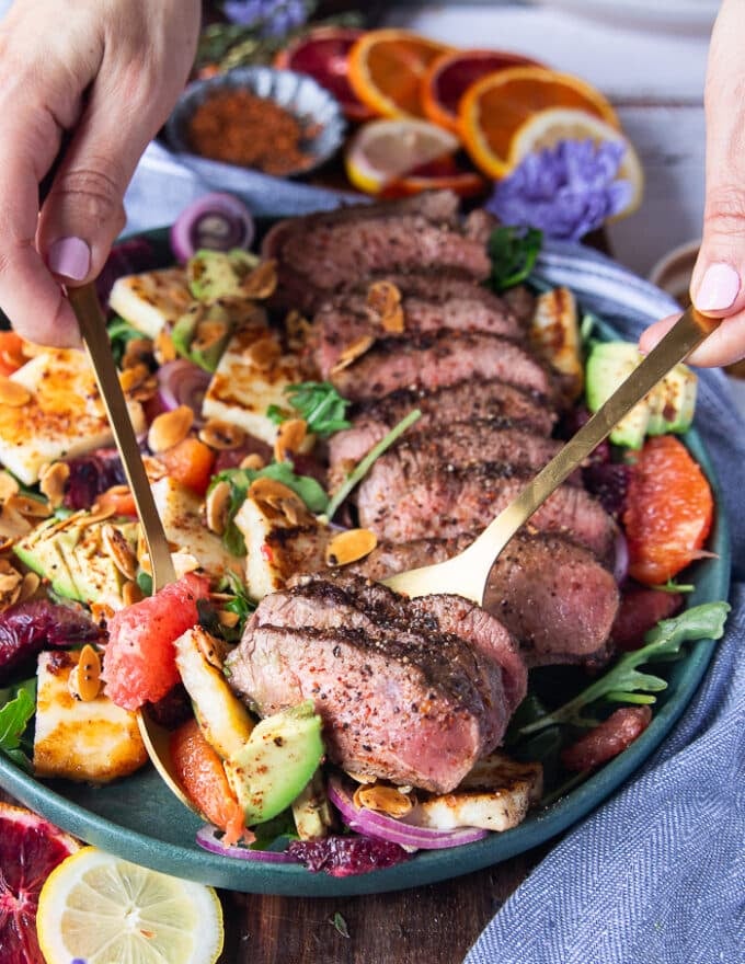 A hand serving the lamb loin recipe and salad using two spoons showing close up the salad and lamb 