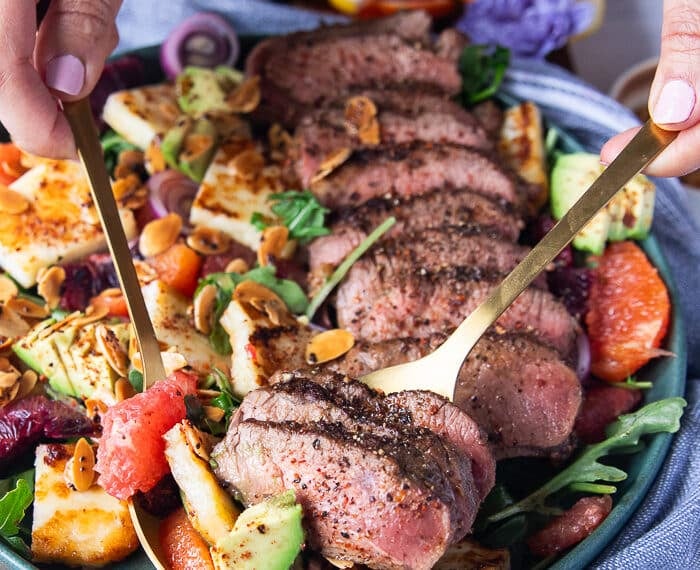 A hand serving the lamb loin recipe and salad using two spoons showing close up the salad and lamb