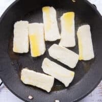 sliced halloumi in a skillet with olive oil searing