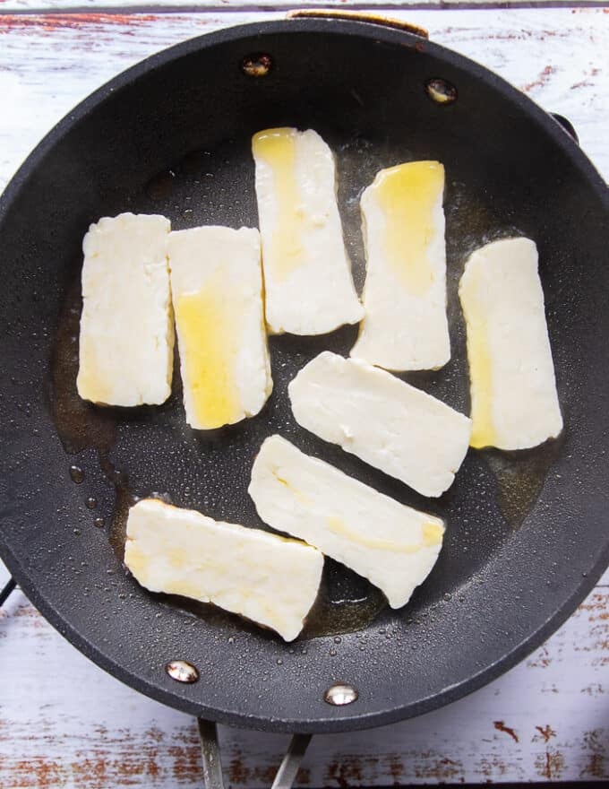 sliced halloumi in a skillet with olive oil searing 