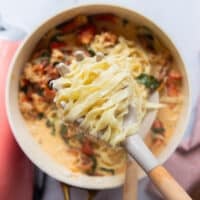 A pasta scoop adding in freshly cooked fettuccine into the creamy lobster sauce skillet