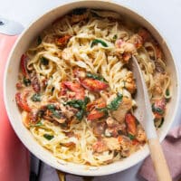 Perfect lobster pasta in a skillet with a creamy sauce with a serving spoon on the side.