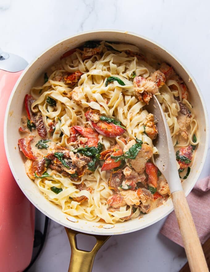 Perfect lobster pasta in a skillet with a creamy sauce with a serving spoon on the side. 