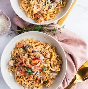 two lobster pasta bowls garnished with parmesan cheese and surrounded by golden cutlery. The pasta is creamy and divine with cooked lobster meat on top