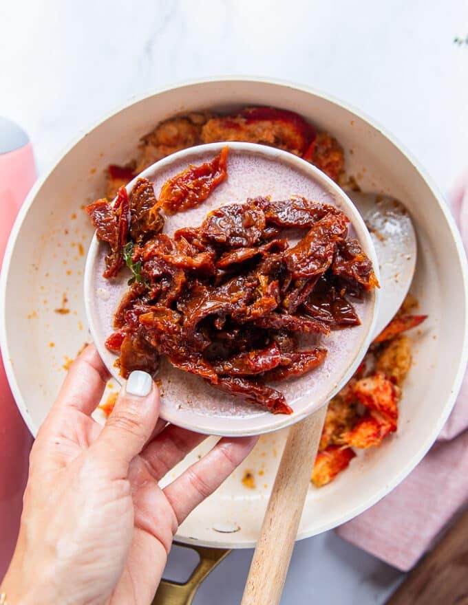 A hand holding a cup of sun dried tomatoes ready to add it to the lobster 