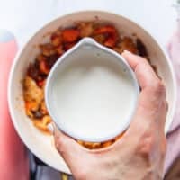 A hand pouring in the cream over the lobster to make the creamy pasta sauce