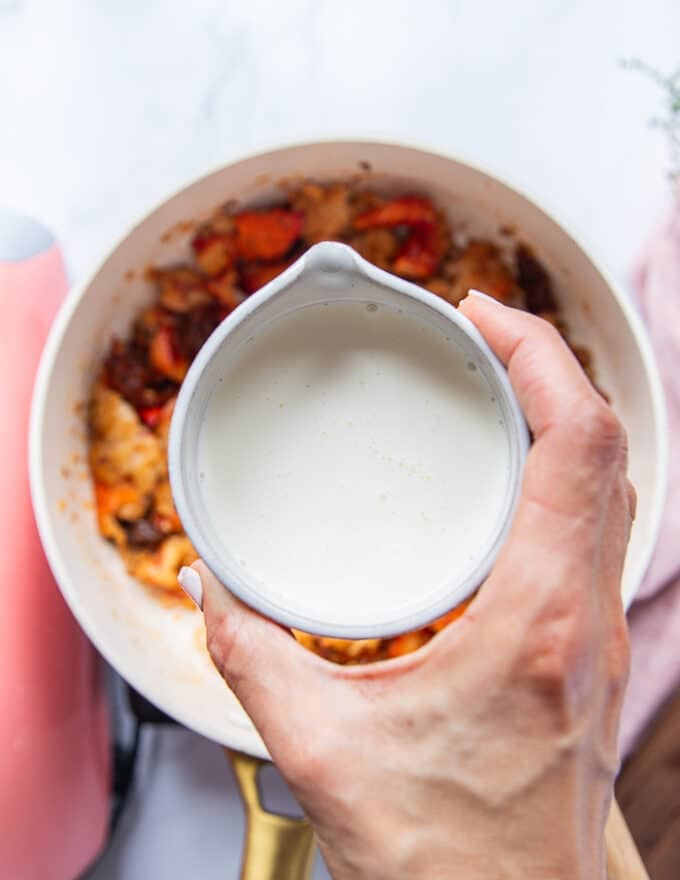 A hand pouring in the cream over the lobster to make the creamy pasta sauce 