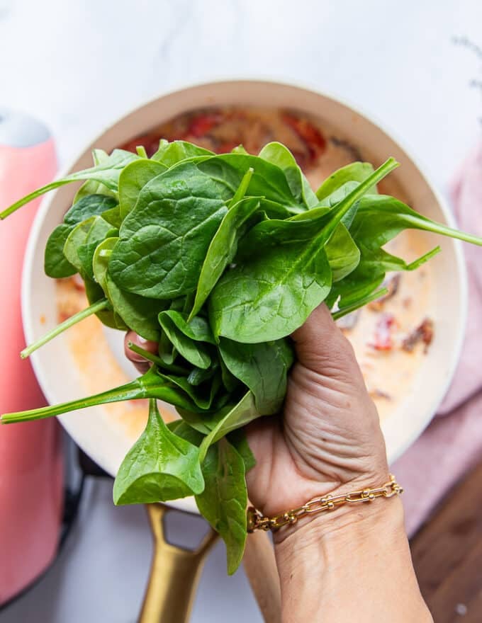 A hand holding the fresh baby spinach to add it to the lobster sauce