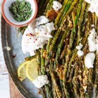 Close up of roasted asparagus sprinkled with parmesan and herbs, chilli flakes on a plate served along side some burrata cheese