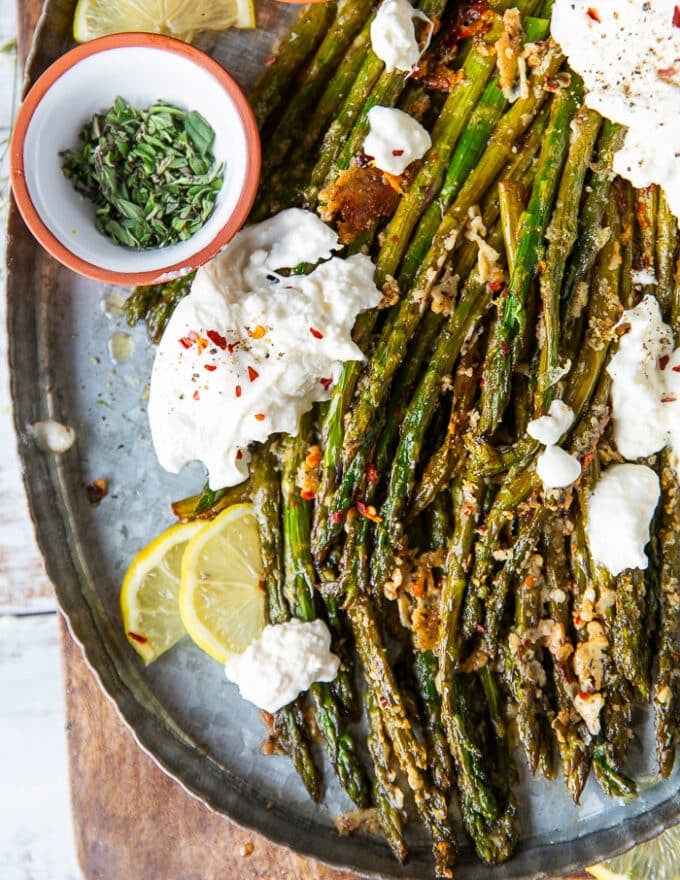 Close up of roasted asparagus sprinkled with parmesan and herbs, chilli flakes on a plate served along side some burrata cheese