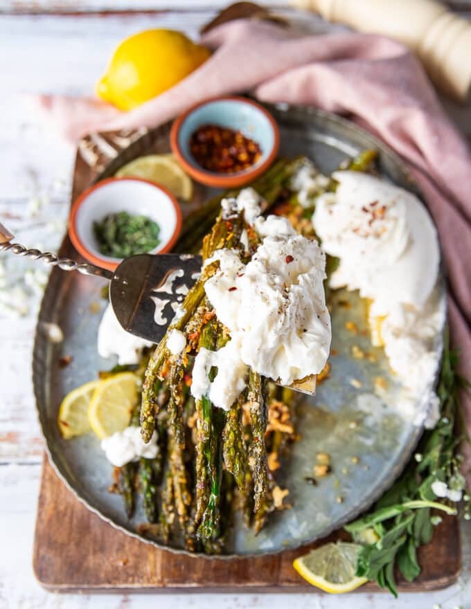 A serving spoon scooping out heaping spoons of the roasted asparagus and burrata cheese close up
