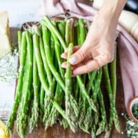 A hand holding one asparagus showing where it has snapped so that way you can trim the whole bunch