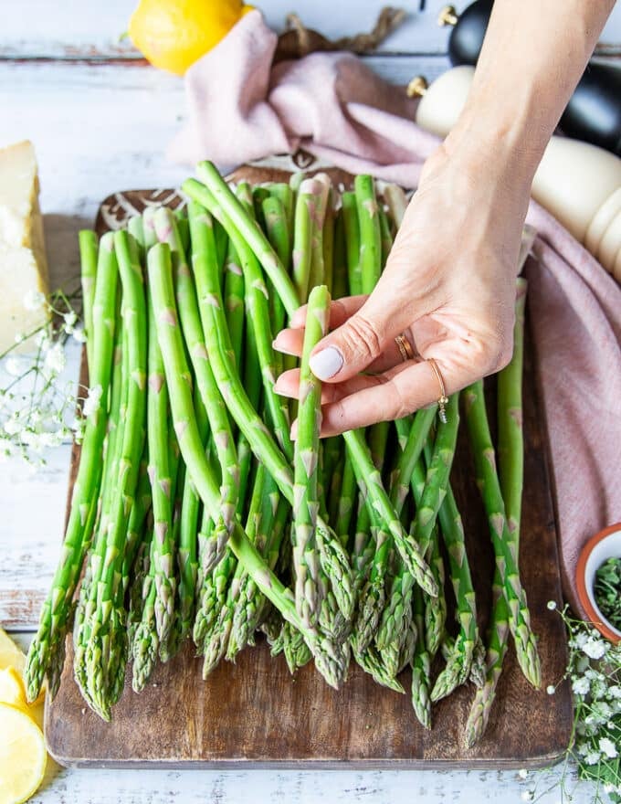 A hand holding one asparagus showing where it has snapped so that way you can trim the whole bunch