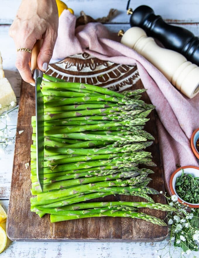 A hand trimming the asparagus using a knife to cut off the tough stems 
