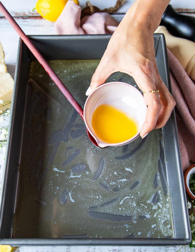 A hand pouring some melted butter at the bottom of a baking pan