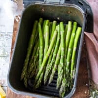 The trimmed asparagus placed in an air fryer basket sprayed with oil, salt and pepper.