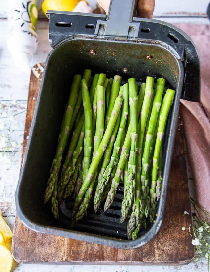 The trimmed asparagus placed in an air fryer basket sprayed with oil, salt and pepper.