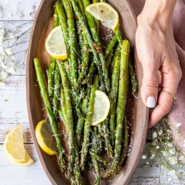A hand holding a serving plate of Air Fryer Asparagus garnished with lemon slices