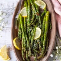 A plated Air fryer asparagus on a wooden plate with lemon slices and parmesan grated on top