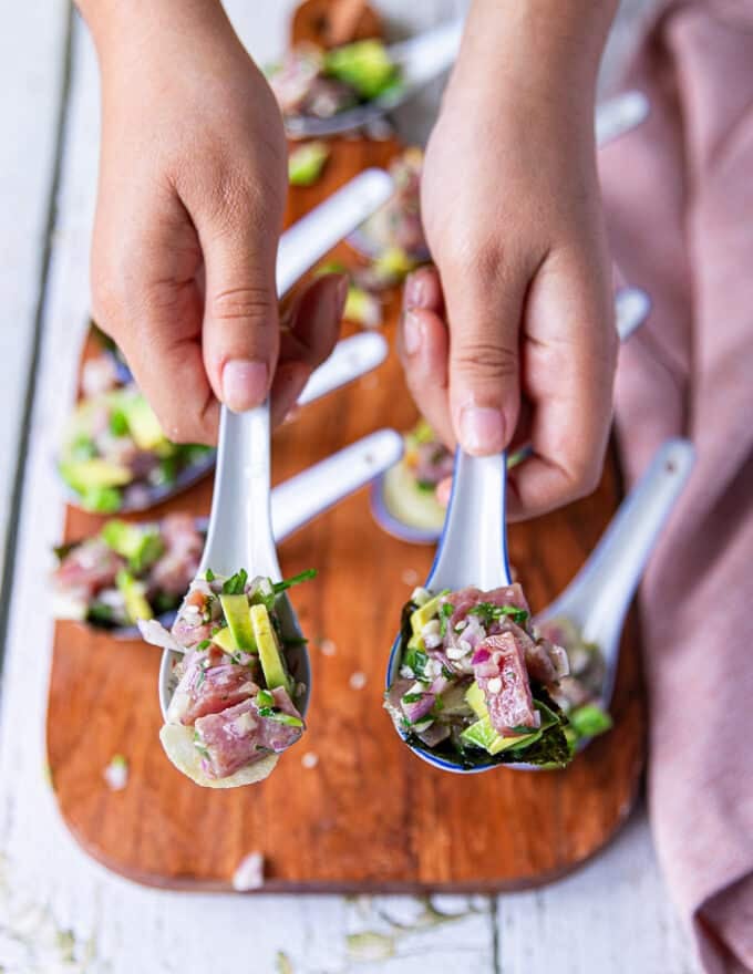 A hand holding spoonfuls of tuna ceviche served with chips