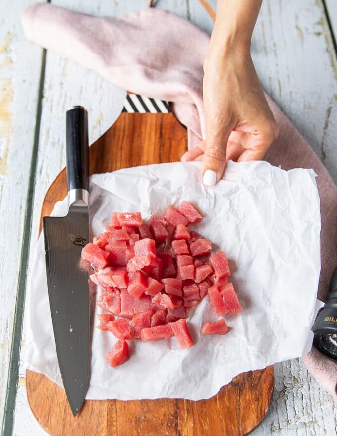 A hand chopping the fresh tuna into half an inch size cubes on a cutting board 