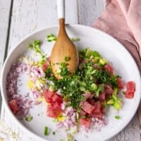 All the ingredients for the tuna ceviche are added into a shallow plate: diced avocados , jalapenos, green onions, red onions, cilantro, lime juice, garlic, olive oil