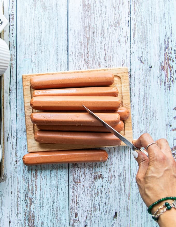 A hand holding a sharp knife and scorching the hot dogs on a diagonal to make like spirals on the side