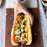 An assembled Chicago style hot dog showing the grilled hot dog with pickled peppers, sliced tomatoes, spicy mayo, jalapenos, minced onions