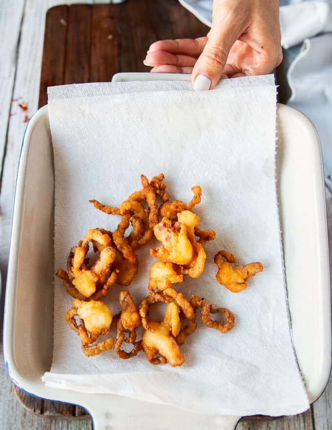 A hand holding a plate lined with paper towel and the fired fish is drying over the paper towels 