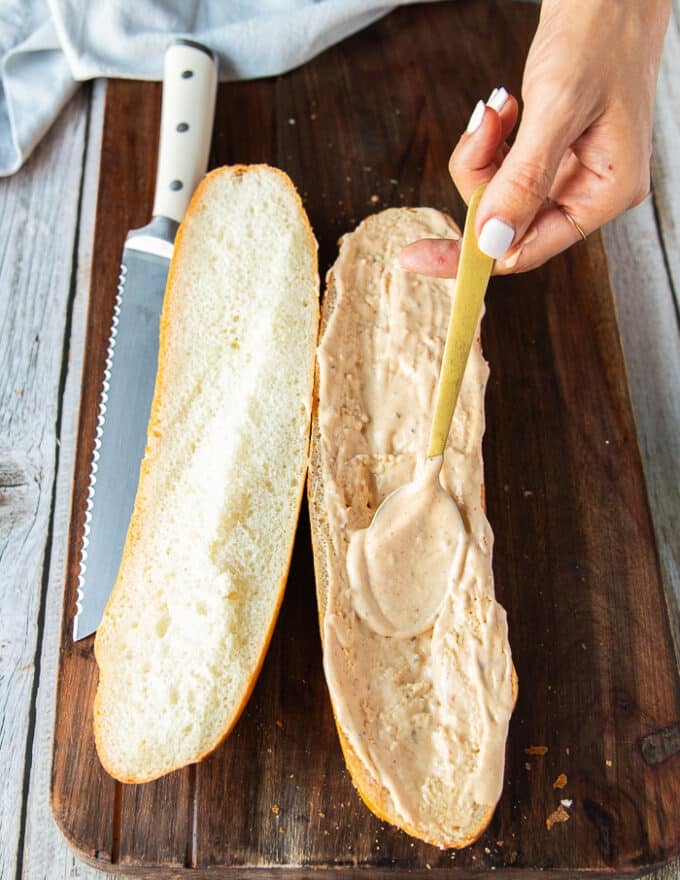 A hand spreading the special remoulade mayo over the french foot long sandwich bread cut in half. 