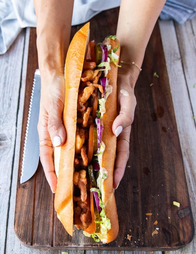 A hand pressing in the other half of the sandwich bread over the fried fish to press in the Po Boy sandwich 