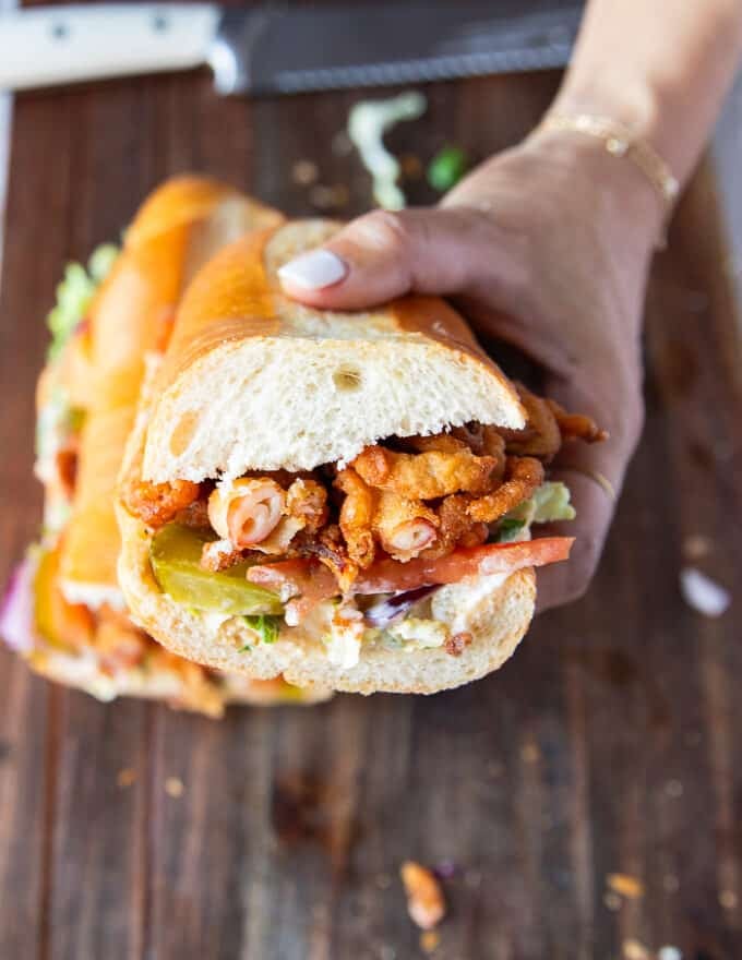 Po Boy Sandwich cut in half showing close u the texture and layers of sauce, lettuce tomatoes, pickles, onions and fried shrimp 