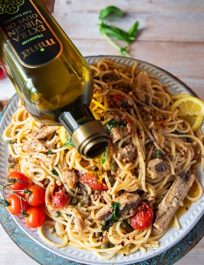 A hand pouring lots of olive oil on the top of the sardine pasta for a final touch