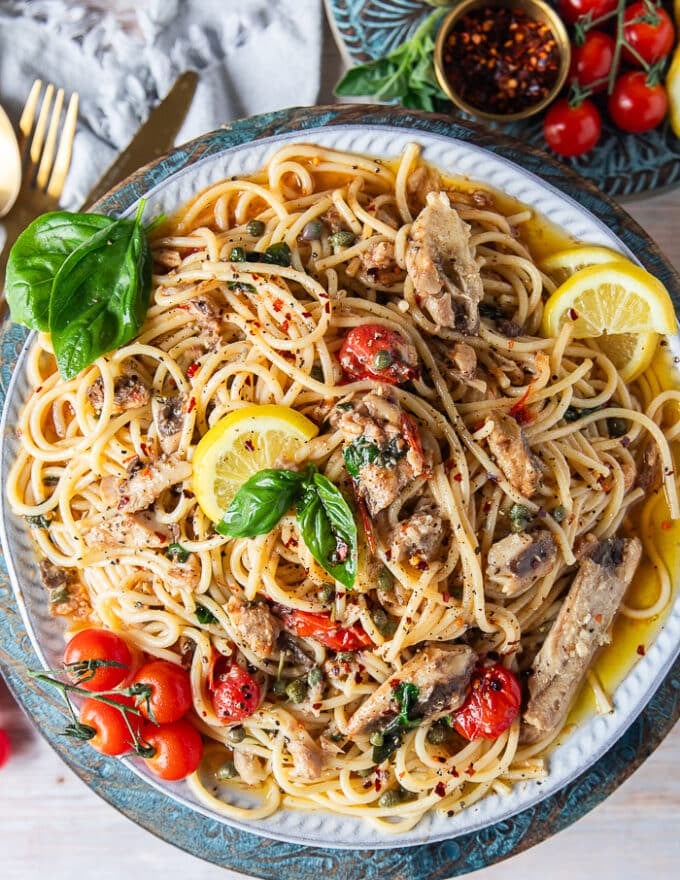 Tope view close up of the finished sardine pasta recipe showing the sardines, pasta, capers, tomatoes, olive oil, lemon zest and lots of lemon slices around