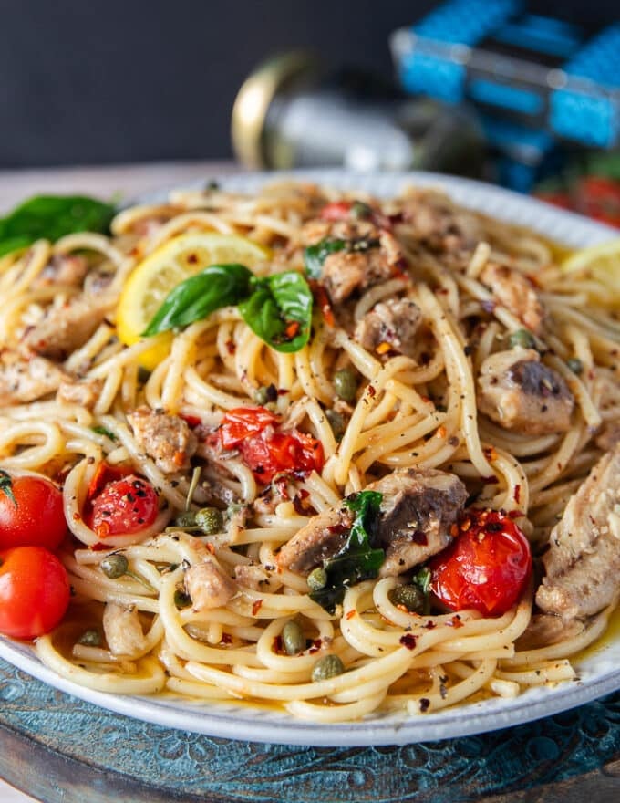 Side view close up of sardine pasta showing the sardines, blistered tomatoes, basil, lemon zest, olive oil