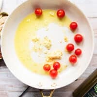 making sardine pasta sauce showing a skillets with lots of olive oil, garlic and cherry tomatoes cooking