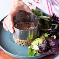 A hand gently lifting the mold showing the beef tartare so beautifully stacked and round