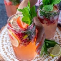A hand holding a fully garnished cup of strawberry mojito close up showing the garnish, the drink