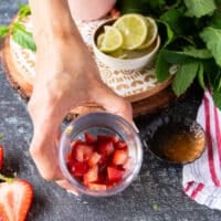A hand holding a cup with diced strawberries to make strawberry mojito