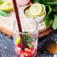 A wooden spoon muddling in the strawberries, mint and lime at the bottom of the cup to make the mojito recipe